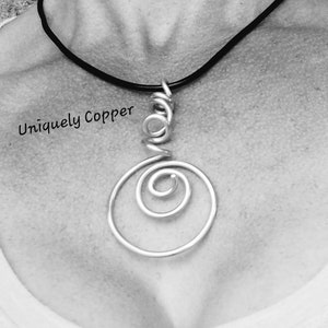 May include: A silver wire necklace with a pendant featuring a spiral design. The necklace is on a black cord.