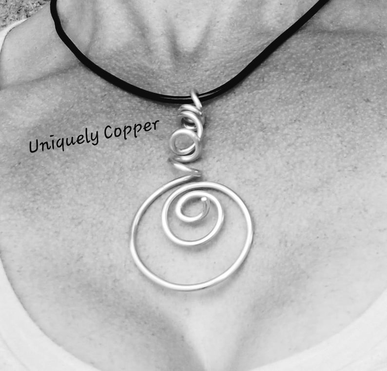 May include: A silver wire necklace with a pendant featuring a spiral design. The necklace is on a black cord.