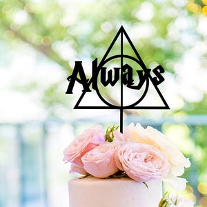 Könnte beinhalten: Eine vierstöckige Hochzeitstorte, verziert mit rosa und cremefarbenen Rosen. Ein schwarzer Tortenaufsatz mit dem Wort "Always" und einem Symbol der Heiligtümer des Todes ist oben platziert. Die Torte steht auf einem silbernen Tortenständer.