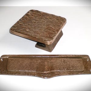 Peut inclure: Ensemble de quincaillerie de porte en bronze, comprenant une poignée carrée texturée et une plaque de fente pour le courrier rectangulaire. L'ensemble a un aspect rustique et vieilli.