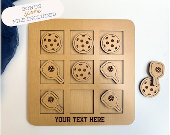 Op de afbeelding: Een houten tic-tac-toe-spelbord met een pickleball-thema. Het bord heeft negen vakjes en is gegraveerd met pickleball-paddles en ballen. Het bord is gepersonaliseerd met de tekst "YOUR TEXT HERE".
