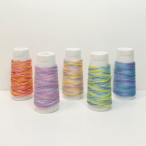 May include: Five spools of colorful embroidery floss, each with a white label that reads "cosmo". The floss is wound around white plastic spools. The colors of the floss are orange, pink, light blue, yellow, and purple.