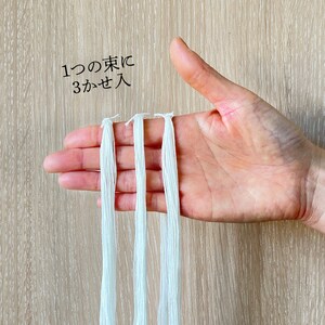 Puede incluir: Tres hebras de hilo de bordar blanco sostenidas en una mano. El texto "1つの束に3かせ入" est&aacute; escrito en la imagen.