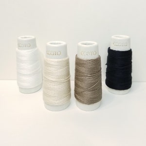 May include: Four spools of thread on white bobbins. The thread colors are white, off-white, brown, and black. The bobbins are labeled "cosmo" in gold lettering.