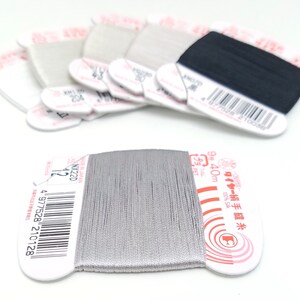 May include: A spool of silver thread with a white label that reads "ワイヤー絹手縫糸 9号 40m プラ 100% Sik" and a barcode. The label also has a red circle with a white letter "C" inside.