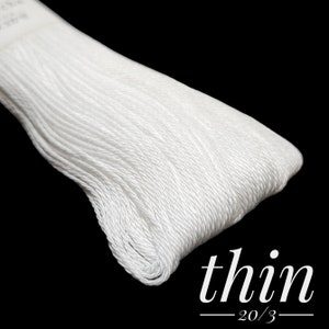 Puede incluir: Primer plano de una bobina de hilo de bordar blanco etiquetada como "thin 20/3".