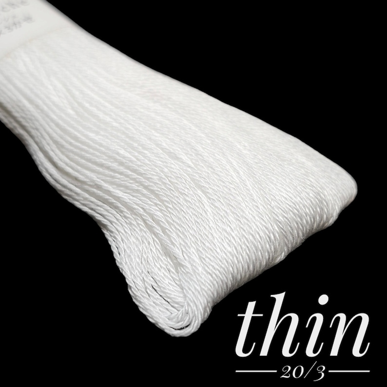 Puede incluir: Primer plano de una bobina de hilo de bordar blanco etiquetada como "thin 20/3".