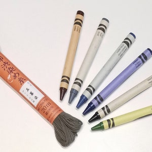 May include: A spool of dark gray embroidery floss with Japanese text on the label, and six crayons in various colors, including brown, gray, blue, indigo, black, and green.