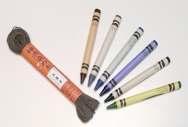 May include: A spool of dark gray embroidery floss with Japanese text on the label, and six crayons in various colors, including brown, gray, blue, indigo, black, and green.