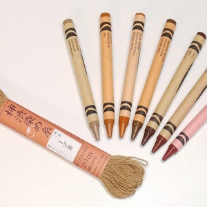 May include: A set of seven brown crayons arranged in a semi-circle with a spool of brown thread and a label that reads "柿渋染め糸子茶 100 6(20s&times;6) 20m 100% send tunal cotto&ntilde;o amarato Bronceado".