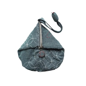 以下が含まれることがあります： 白ステッチの幾何学模様が施された、デニム色の三角形の小銭入れ。 銀色の留め金と、赤ステッチの小さな丸いボタンが付いています。 小さな丸いデニム色のビーズが細いストラップで取り付けられています。