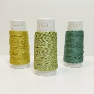 May include: Three spools of thread in green, yellow, and a darker green. The spools are labeled "cosmo" in gold lettering.