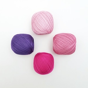 May include: Four balls of yarn in different shades of pink and purple. The yarn is wound into balls and ready for knitting or crocheting.