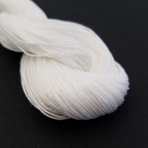 May include: A skein of white yarn, tightly wound and textured, against a dark background. The yarn appears soft and fluffy, ideal for knitting or crocheting projects. The close-up shot highlights the fine strands.