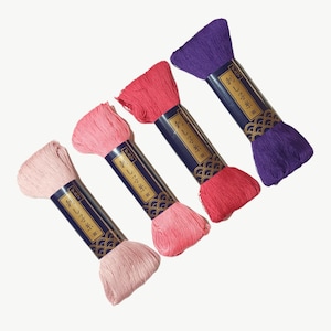 May include: Four spools of embroidery floss in shades of pink, red, and purple. Each spool has a blue label with Japanese text and a gold design.
