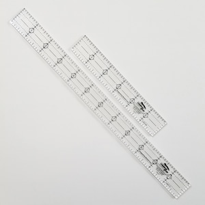 Könnte beinhalten: Zwei transparente Plastiklineale mit schwarzen Markierungen. Die Lineale sind in Zoll unterteilt und haben ein Rastermuster. Die Lineale werden von Creative Grids hergestellt.