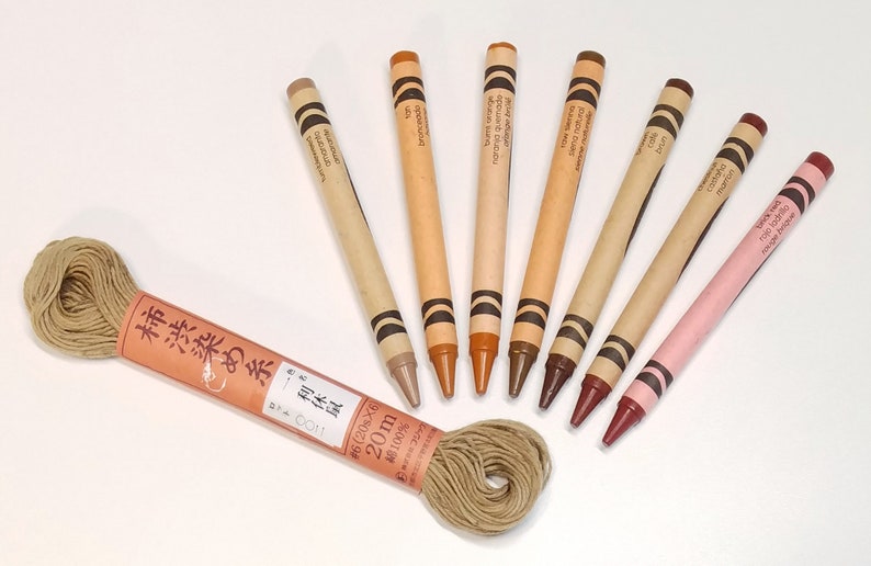 May include: A spool of 20 meters of 100% cotton thread in a natural beige color, labeled "柿渋染め糸体 0011 omaranto #6(20g&times;6) 20m 綿100%".  The thread is surrounded by eight crayons in various shades of brown, beige, and pink.