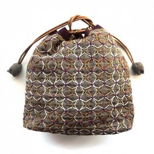 May include: A brown drawstring bag with a geometric pattern embroidered in white, gold, and purple thread. The bag has a brown leather drawstring and a purple lining.