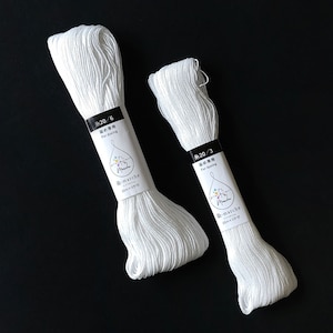 Puede incluir: Dos carretes de hilo de algod&oacute;n blanco para te&ntilde;ir, etiquetados con "糸20/6 染め専用 For dyeing -marche 20m&times;3かせ" y "糸20/3 染め専用 For dyeing -marche 20m&times;3かせ".