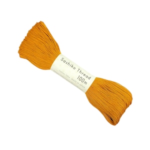 May include: A spool of 100 meter yellow sashiko thread, a type of Japanese embroidery thread, with a label that reads "Sashiko Thread 100m Cotton 100% MADE IN JAPAN https://olympus-thread.com"
