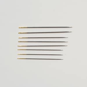 May include: A set of eight silver sewing needles with gold tips. The needles are arranged vertically in a row.