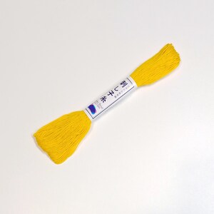 May include: A spool of yellow embroidery floss with a white label that reads "糸  (いと)  綿  (わた)  100%" and "米  (こめ)  型  (がた)"