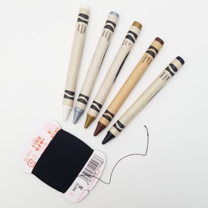 May include: A set of ten crayons in various colors, including white, silver, gold, brown, and black. The crayons are labeled with their color names in English, Spanish, and French. The crayons are arranged in a row on a white surface.