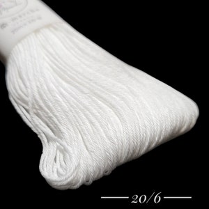 Puede incluir: Primer plano de una bobina de hilo de bordar blanco con el texto "20/6" impreso en la etiqueta.