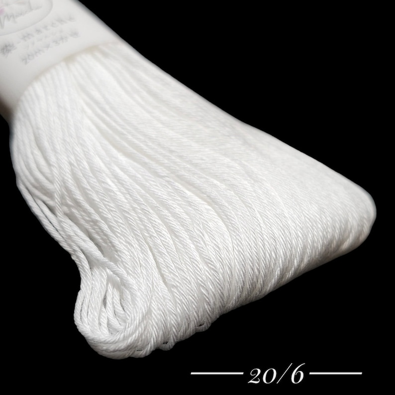Puede incluir: Primer plano de una bobina de hilo de bordar blanco con el texto "20/6" impreso en la etiqueta.