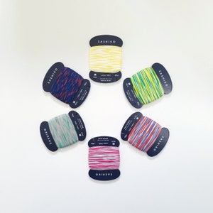 May include: Six spools of colorful embroidery floss, each with a black label that reads "SASHIKO" and includes details about the thread, such as the material, length, and origin.