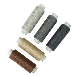 May include: An assortment of spools of thread in various colors, including gray, brown, and beige. Each spool is cylindrical with a white base and a label. The threads are tightly wound, showcasing a textured appearance. The image is set against a plain white background.