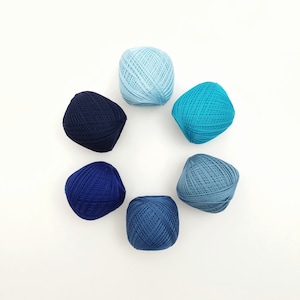 May include: A collection of six balls of yarn in varying shades of blue, arranged in a circular pattern on a white background. The colors range from light sky blue to deep navy, showcasing a gradient effect. Ideal for knitting or crochet projects.