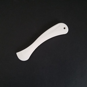 May include: A white plastic curved sewing tool with a rounded end and a hole at the other end. The tool has the word "CLOVER" printed on it. The tool is on a black background.