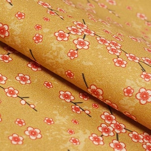 May include: A close-up of a mustard yellow fabric with a repeating pattern of small white and red flowers. The fabric is folded in half, showing the pattern on both sides.