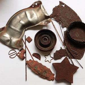May include: A collection of rusty metal scraps, including a large curved piece, a smaller circular piece, a star shape, and a few smaller pieces. The scraps are arranged in a circle on a white background.
