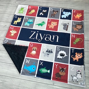 May include: A blue and red alphabet blanket with a personalized name "Ziyan" in white. The blanket features a different animal for each letter of the alphabet.