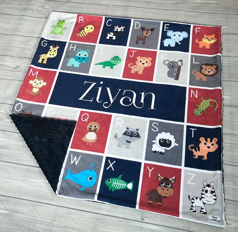 May include: A blue and red alphabet blanket with a personalized name "Ziyan" in white. The blanket features a different animal for each letter of the alphabet.