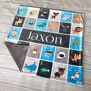 May include: A blue and gray baby blanket with an alphabet design featuring animals. The blanket has a soft, minky backing and is personalized with the name "Jaxon".