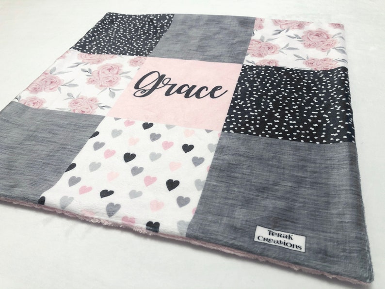May include: A pink and gray patchwork baby blanket with a floral pattern, hearts, and polka dots. The blanket is personalized with the name "Grace".