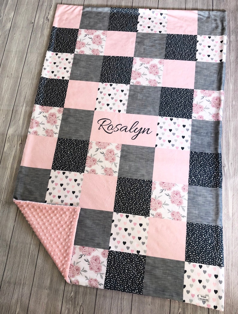 May include: A pink and gray patchwork baby blanket with a floral and heart print. The blanket is personalized with the name "Rosalyn".
