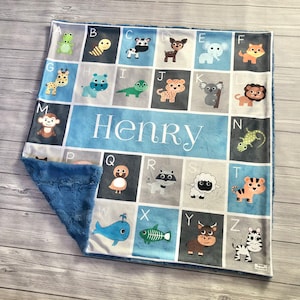 May include: A blue and gray baby blanket with a personalized name "Henry" in white letters. The blanket features an alphabet design with animal illustrations for each letter.