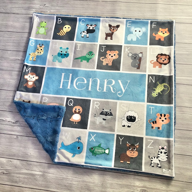 May include: A blue and gray baby blanket with a personalized name "Henry" in white letters. The blanket features an alphabet design with animal illustrations for each letter.
