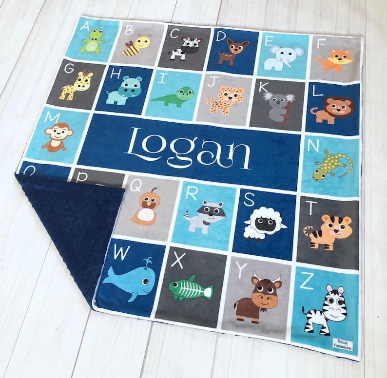 May include: A blue and gray alphabet blanket with a personalized name "Logan" in white. Each letter is paired with a different animal illustration.