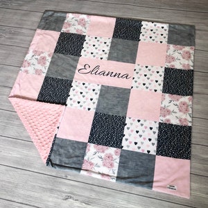 May include: A pink and gray patchwork baby blanket with a floral and heart print. The blanket is personalized with the name "Elianna".