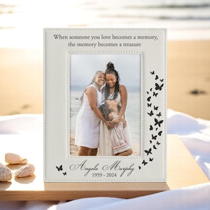May include: A white picture frame with a photo of three people. The frame has the text "When someone you love becomes a memory, the memory becomes a treasure" and "Angela Murphy 1959-2024". Black butterfly accents decorate the frame.