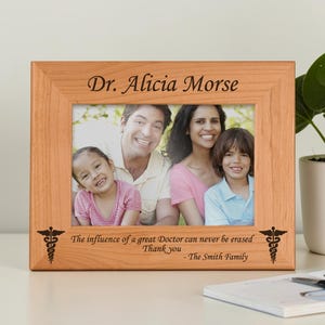 May include: A wooden picture frame with a family photo. The frame is engraved with "Dr. Alicia Morse" at the top and a message of gratitude at the bottom. The frame has a medical symbol on each side.