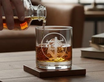 May include: A clear glass tumbler featuring a white etched graphic of a utility pole inside a circle. The glass contains amber-colored liquid and a large ice cube. A matching clear glass decanter is pouring more amber liquid into the tumbler.
