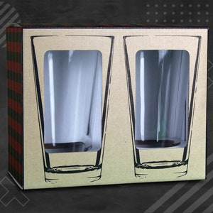 Puede incluir: Una caja de cart&oacute;n con un patr&oacute;n de cuadros en el lateral. La caja contiene dos vasos de pinta de vidrio transparente. Los vasos son visibles a trav&eacute;s de ventanas recortadas en la caja.