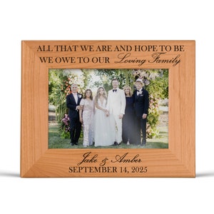 May include: A light brown wooden picture frame with engraved text reading ALL THAT WE ARE AND HOPE TO BE WE OWE TO OUR Loving Family at the top and Jake & Amber SEPTEMBER 14, 2025 at the bottom, containing a photo of six people.