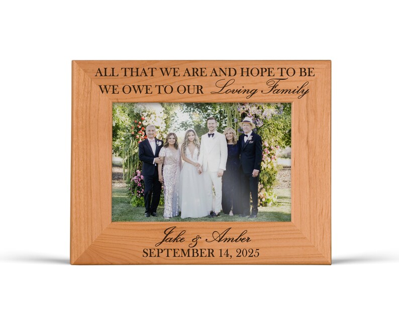 May include: A light brown wooden picture frame with engraved text reading ALL THAT WE ARE AND HOPE TO BE WE OWE TO OUR Loving Family at the top and Jake & Amber SEPTEMBER 14, 2025 at the bottom, containing a photo of six people.